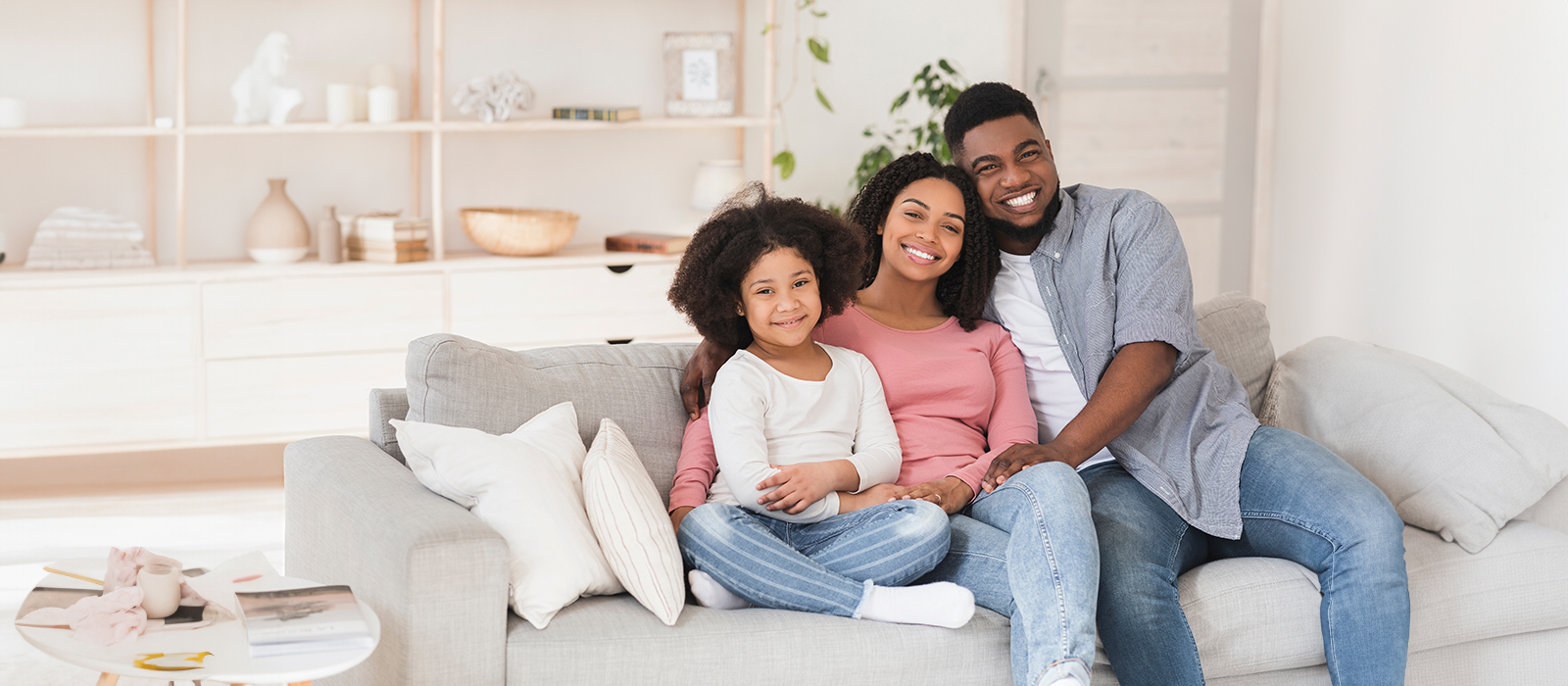 A family of four, including two adults and two children, poses for a photo on a couch in a modern living room.